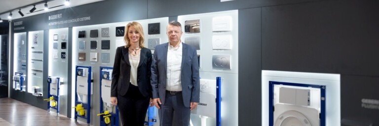 Zwei Personen stehen in einem Ausstellungsraum vor einer Wand mit Sanitärsystemen und Produkten der Marke Geberit.