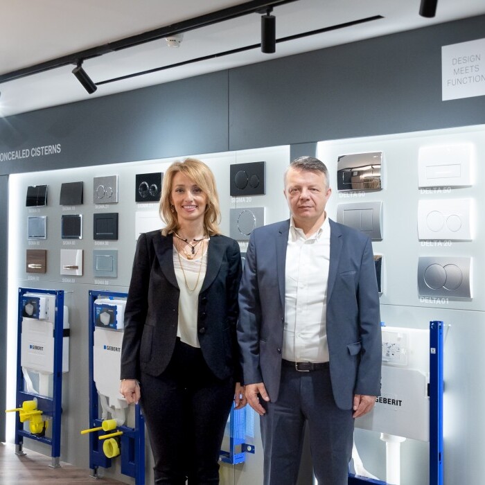 Zwei Personen stehen in einem Ausstellungsraum vor einer Wand mit Sanitärsystemen und Produkten der Marke Geberit.