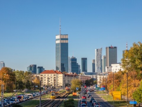 City skyline featuring modern skyscrapers, a clear blue sky, and autumn foliage along the road.