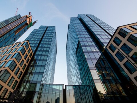 Two modern glass skyscrapers viewed from below, reflecting the sky, with construction elements visible on one.