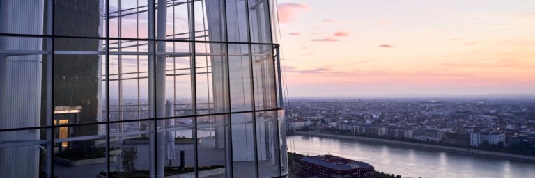 View from a high-rise building featuring glass architecture, overlooking a river and city skyline at sunset.