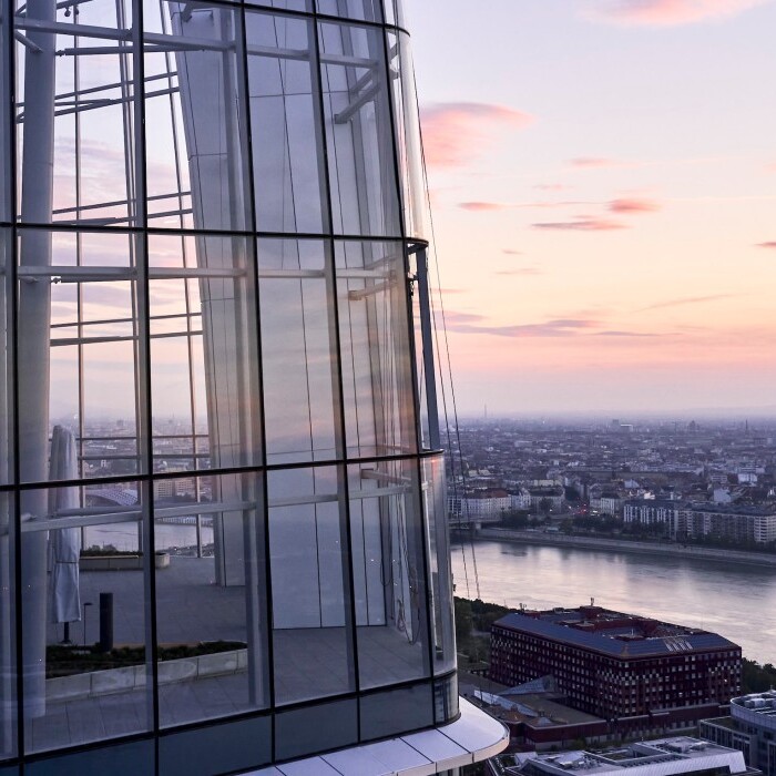 View from a high-rise building featuring glass architecture, overlooking a river and city skyline at sunset.