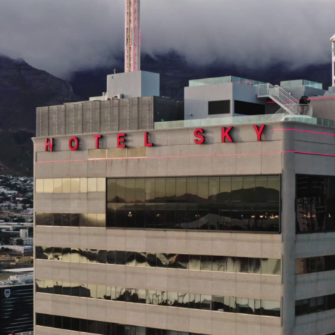 A modern high-rise building labeled "Hotel Sky," surrounded by urban structures and mountains in the background.