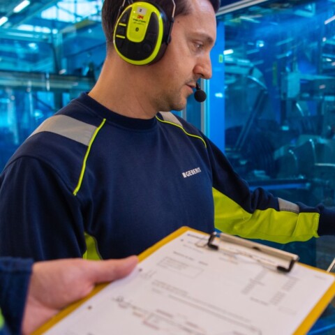 A man wearing headphones operates a control panel in an industrial setting.