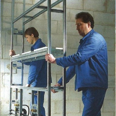 Zwei Männer in blauen Arbeitsanzügen arbeiten an einem Gerüst in einem unbehandelten Raum.