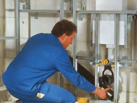 Ein Handwerker in blauer Arbeitskleidung, der an einem Rohrsystem arbeitet.