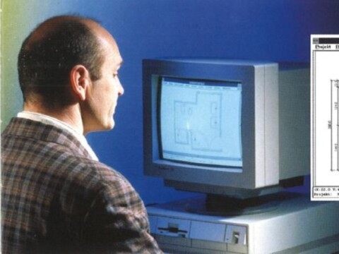 Ein Mann in einem karierten Anzug sitzt vor einem alten Computerbildschirm, der einen Grundriss zeigt.