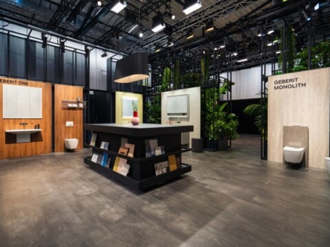 Moderne Ausstellung mit verschiedenen Badezimmerdesigns, einer zentralen Informationsinsel und Pflanzen im Hintergrund.