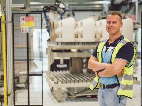 Ein lächelnder Mann in Sicherheitsbekleidung steht in einer Fabrikhalle.