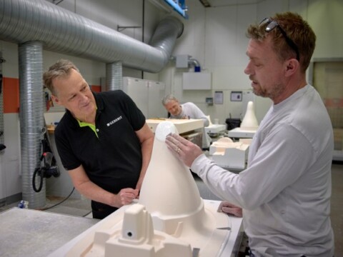 Zwei Personen stehen an einem Tisch in einer Werkstatt um ein helles Bauteil.