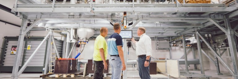 Drei Personen in einem Industrieumfeld betrachten gemeinsam eine technische Anlage.