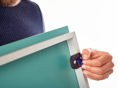 Eine Person hält ein Spiegel mit einem weissen Rahmen und befestigt einen schwarzen Clip am Rahmen.