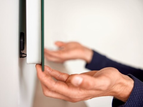 Hände strecken sich, um eine Glasplatte an einer Wand zu halten.