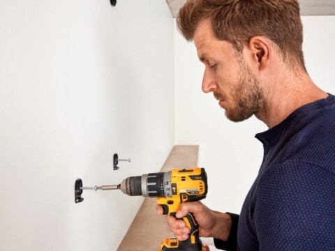 Ein Mann benutzt einen Akku-Bohrschrauber, um eine Halterung an einer weissen Wand zu befestigen.