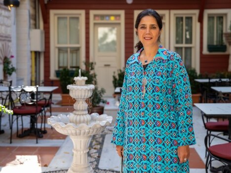 A woman in a colourful patterned dress stands beside a decorative fountain with outdoor seating.
