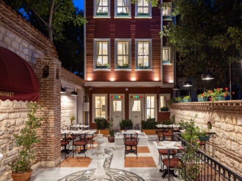 A charming outdoor dining area with tables and chairs set up in front of a lit building, surrounded by greenery.