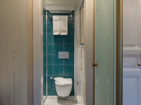 Narrow bathroom with a wall-mounted toilet, turquoise tiled wall, and glass shower door.