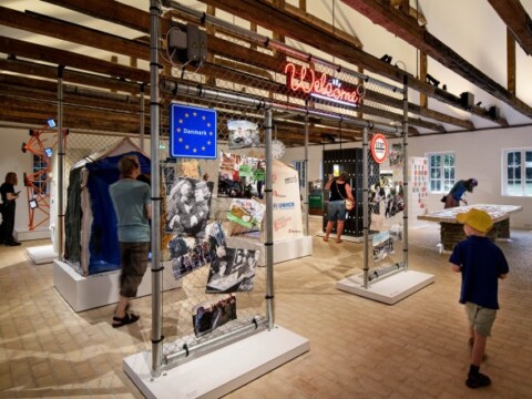 An indoor exhibition space featuring displays with images and signs, where visitors are interacting and observing the exhibits.