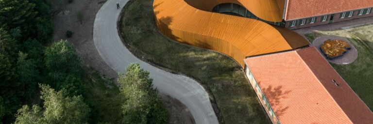 Aerial view of a curved path leading to a modern building with a distinctive orange roof surrounded by trees.