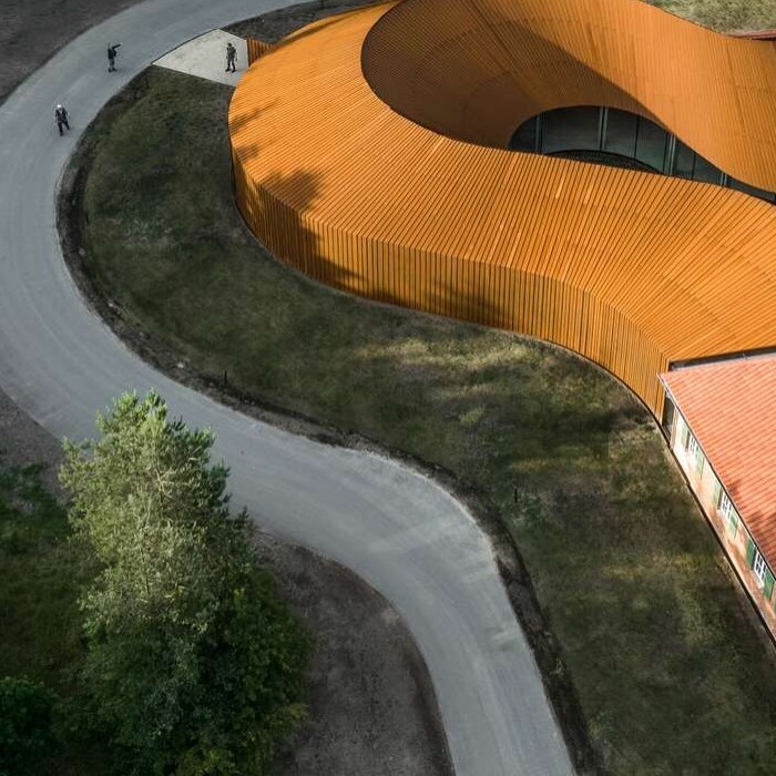 Aerial view of a curved path leading to a modern building with a distinctive orange roof surrounded by trees.