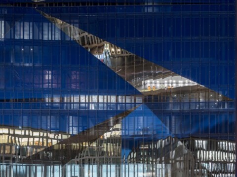 A modern building facade with abstract blue panels and reflective glass sections creating a geometric design.