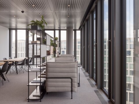 Modern office interior with large windows, seating area, and plants, featuring a minimalist aesthetic.