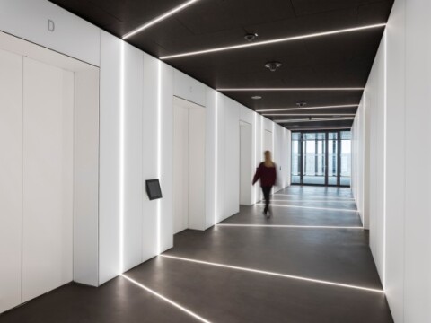 A modern corridor with white walls, elevators on one side, and a person walking.