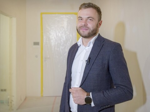 Ein Mann in einem Anzug steht vor einer unvollendeten Innenraum-Wand mit gelber Umrandung.