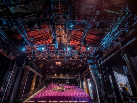 View of a stage with stage lighting and pink seating in a theater setting.