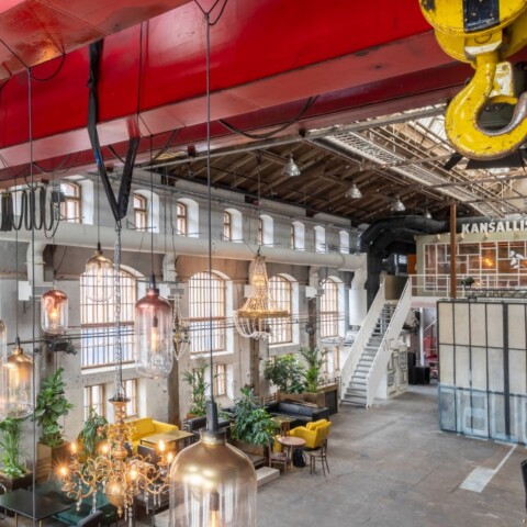 An industrial-style interior featuring large windows, lights, and seating areas with plants.