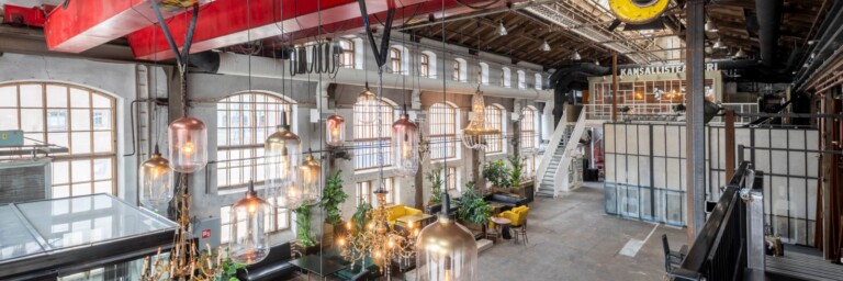 An industrial-style interior featuring large windows, lights, and seating areas with plants.