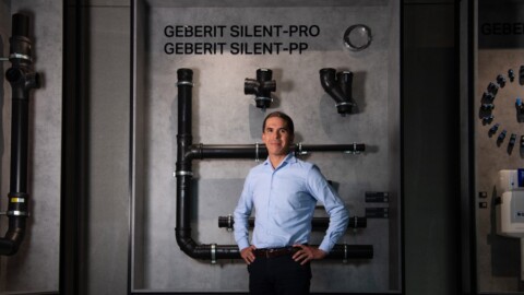 A man stands confidently in front of a display featuring various plumbing pipes labeled Geberit Silent-Pro and Geberit Silent-PP.