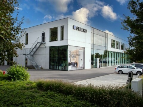 Modern commercial building with large glass windows, greenery in the foreground, and a staircase on the side.