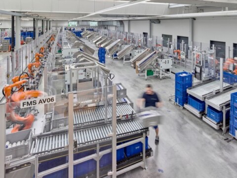A wide view of a modern automated warehouse with conveyor belts, robotic arms, and workstations.