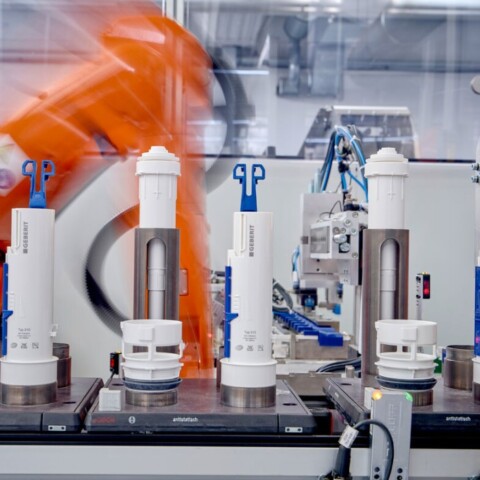 Robotic arms in a factory setting assembling cylindrical components on a conveyor belt.