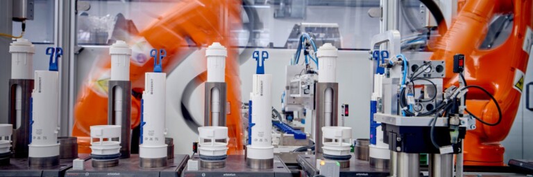 Robotic arms in a factory setting assembling cylindrical components on a conveyor belt.