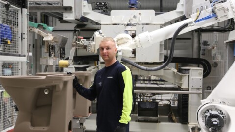 Mann in Arbeitskleidung steht neben einem automatisierten Roboterarm.