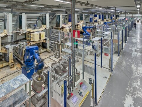 Fertigungshalle mit mehreren Maschinen und Industrieroboter, die durch Sicherheitszäune voneinander getrennt sind.