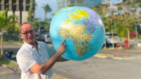 Ein Mann hält einen Globus und zeigt auf den Kontinent Afrika, während er im Freien steht.