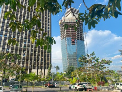Moderne Gebäude mit Glasfassade in der Bauphase, umgeben von Bäumen und Autos.