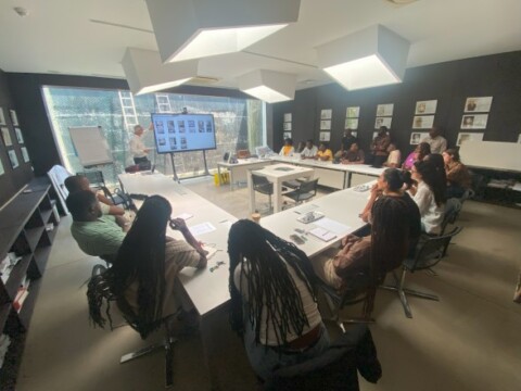 Eine Gruppe von Menschen sitzt in einem modernen Konferenzraum und schaut auf einen Bildschirm, wo Präsentationsinhalte angezeigt werden.