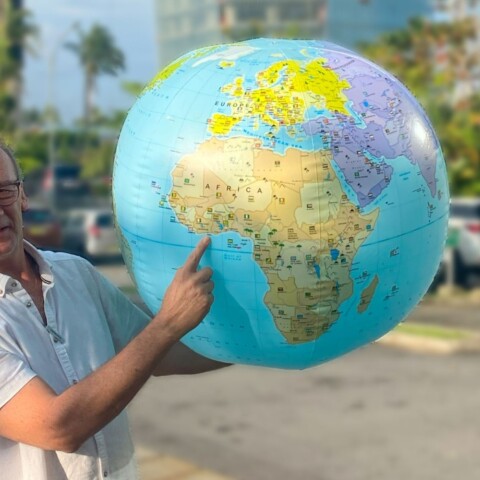 Ein Mann hält einen Globus und zeigt auf den Kontinent Afrika, während er im Freien steht.