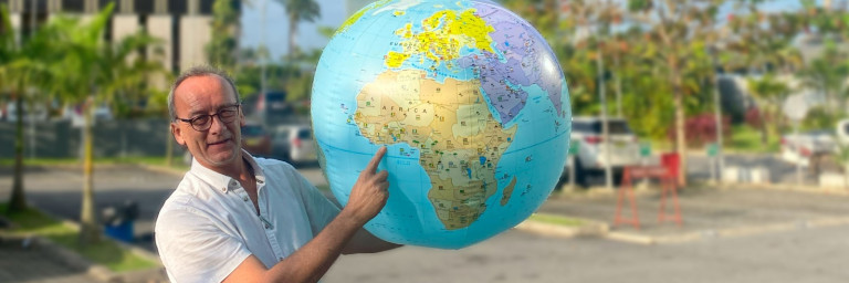 Ein Mann hält einen Globus und zeigt auf den Kontinent Afrika, während er im Freien steht.