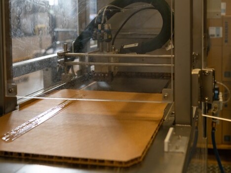 Ein automatisierter Maschinenprozess zum Auftragen von Klebstoff auf eine Kartonschicht.