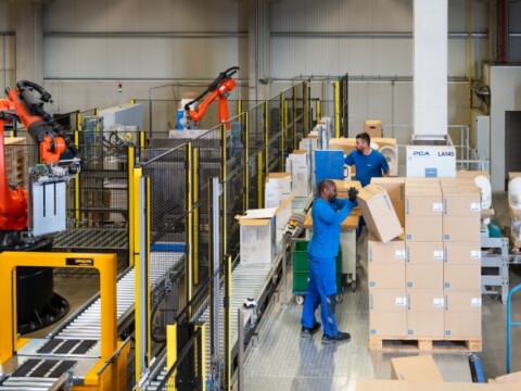 Eine moderne Lagerhalle mit automatisierten Robotern und zwei Mitarbeitern, die Kartons verarbeiten.
