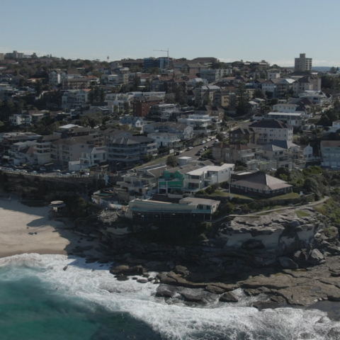 Küstenansicht mit Strand, Wellen und Wohngebieten.