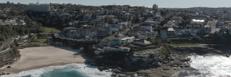 Küstenansicht mit Strand, Wellen und Wohngebieten.