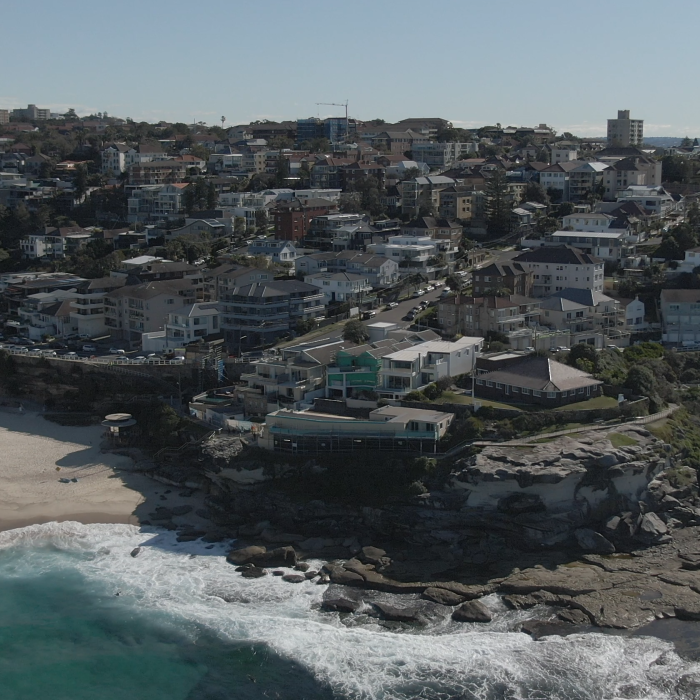 Küstenansicht mit Strand, Wellen und Wohngebieten.