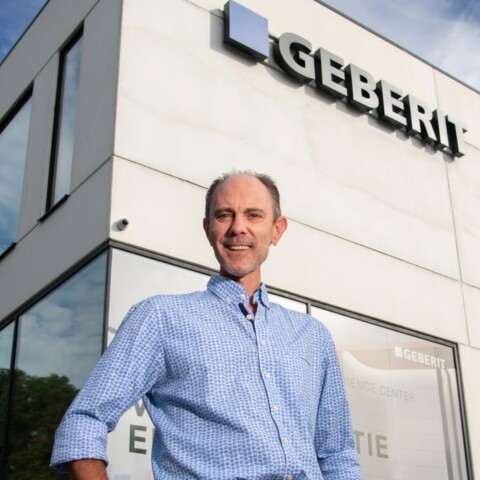 Mann in einem blauen Hemd steht vor einem modernen Firmengebäude mit dem Schriftzug "Geberit".