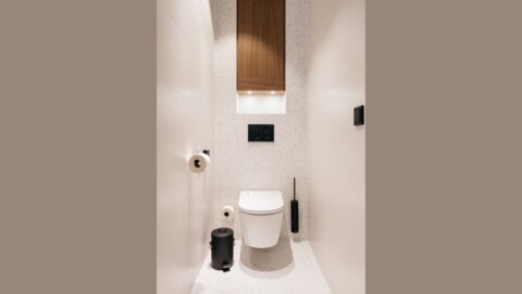 Modernes, minimalistisches Badezimmer mit weisser Wand, Toilette, und Holzregal.